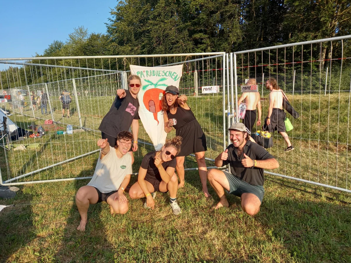 Eine Gruppe von Menschen vor einem Absperrzaun auf einem Festival bei Sonnenuntergang