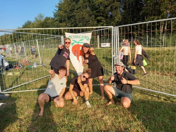 Eine Gruppe von Menschen vor einem Absperrzaun auf einem Festival bei Sonnenuntergang